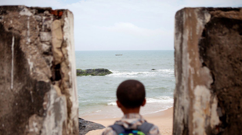 Jasir Robert Ryan-Lee, a descendant of Venture Smith, looks out to the shore from the roof of the fort in Anomabo, Ghana, where his ancestor was held as a slave, then taken to a ship through its Door of No Return. Credit Jane Hahn for The New York Times  